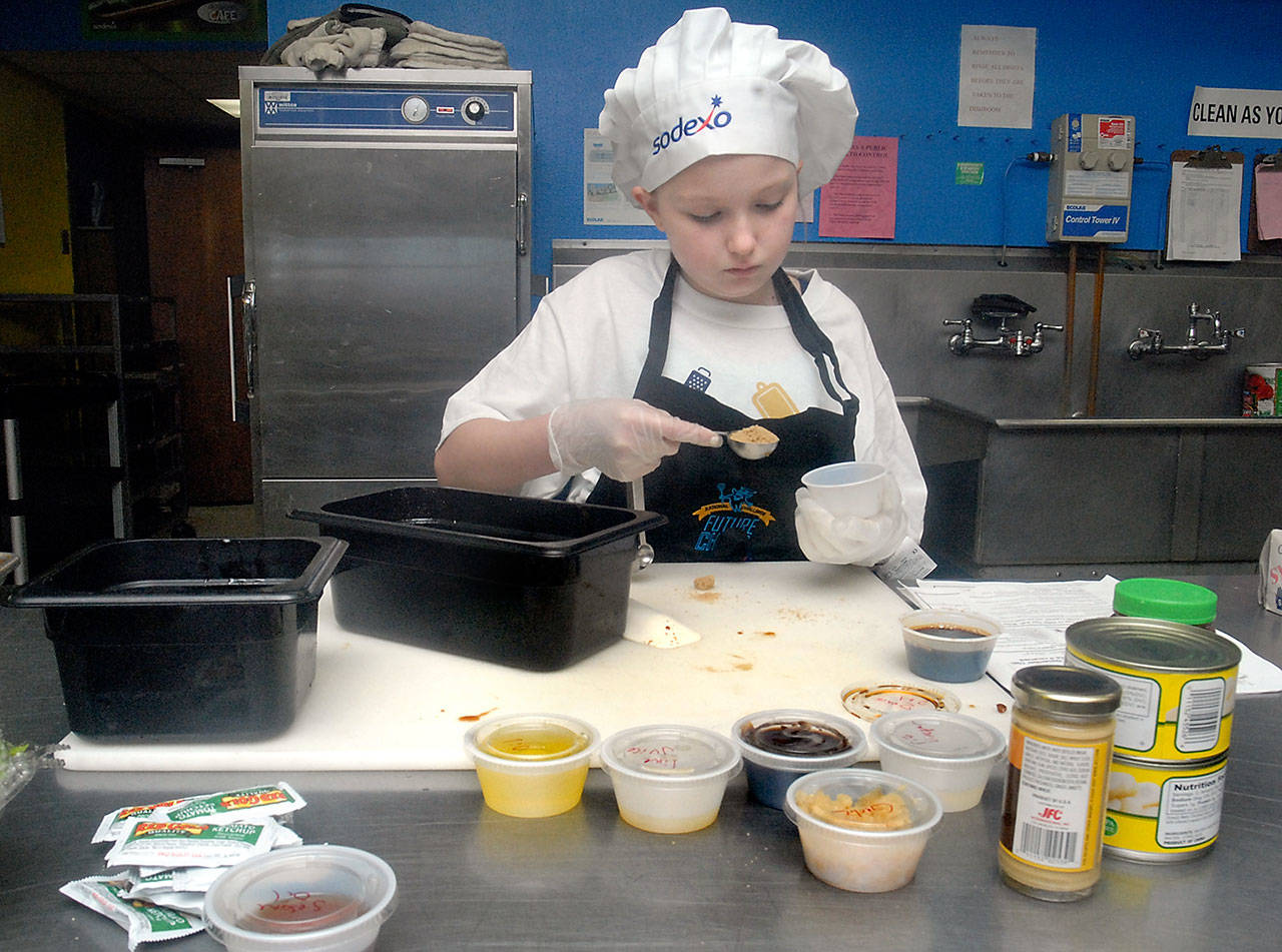 Ten-year-old Domiana Badger, a fifth-grade student at Hamilton School in Port Angeles, adds seasoning for a dish of chicken lettuce wraps, during Friday’s “Kids Can Cook” competition at the Port Angeles High School cafeteria. (Keith Thorpe/Peninsula Daily News)