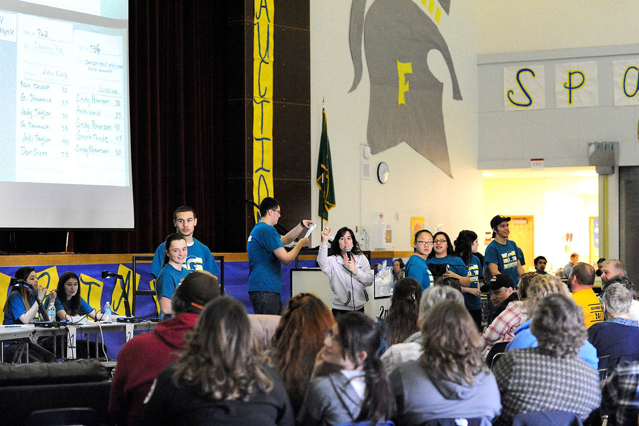 Patty Brandt auctions items over the speakers at the Forks High School commons and also over Forks Broadcasting 96.7 while FHS seniors dressed show items to be auctioned during the 2017 Quillayute Valley Scholarship Auction. (Lonnie Archibald/for Peninsula Daily News)