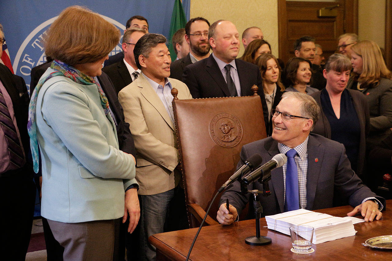 Gov. Jay Inslee, seated, speaks with Democratic Sen. Christine Rolfes, left, before signing the supplemental budget Tuesday in Olympia. (Rachel La Corte/The Associated Press)