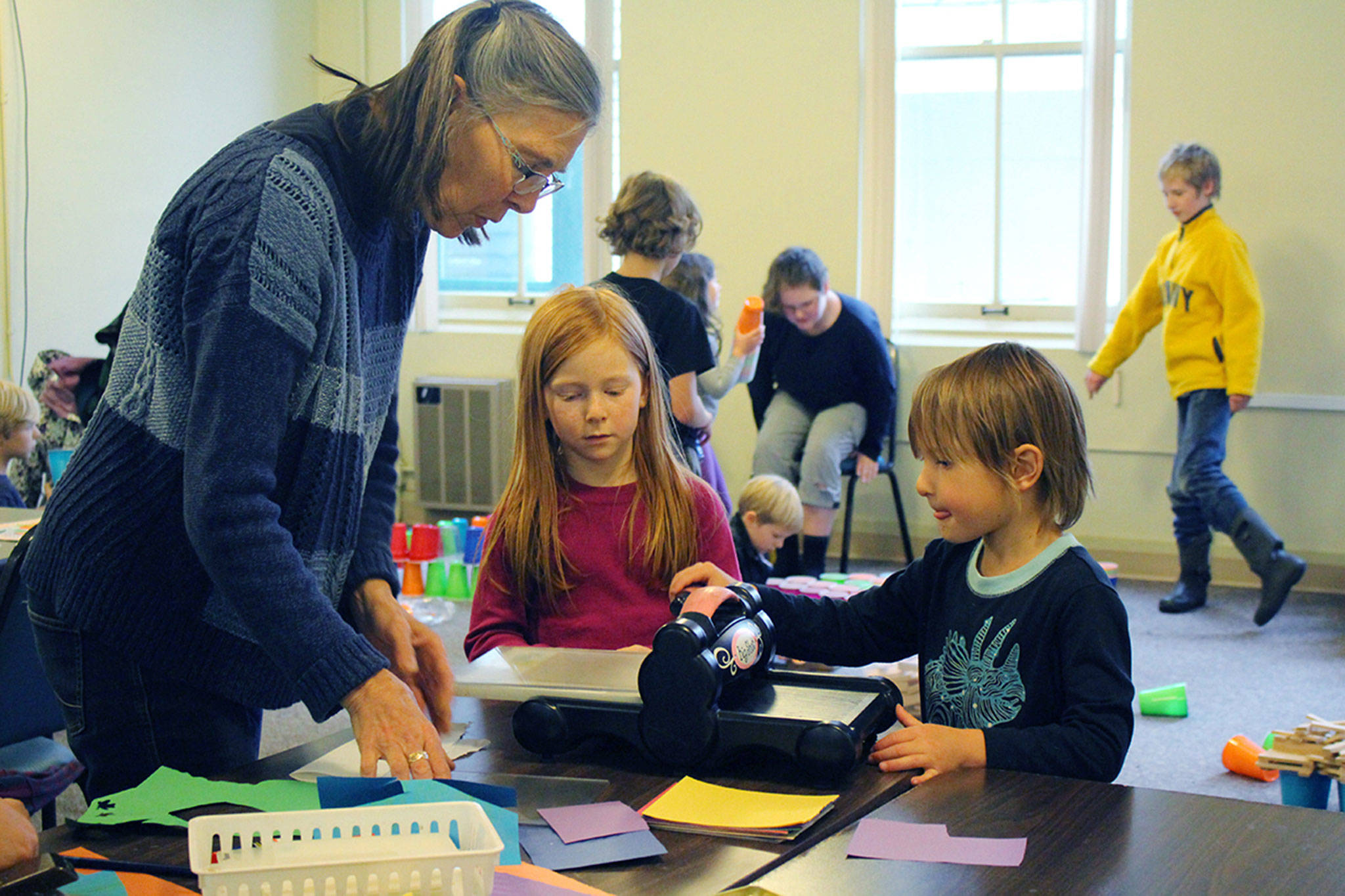 Lead teacher Frances Rice, left, with Alexis Frederickson and Eli Collins, demonstrates how to use a paper press in art studio on Friday in Port Townsend.