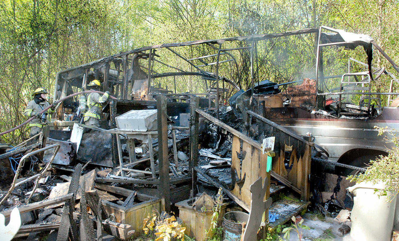 Clallam County Fire District No. 3 firefighters extinguish hot spots from a blaze that destroyed a motor home off Pierson Road west of Sequim on Saturday. (Keith Thorpe/Peninsula Daily News)