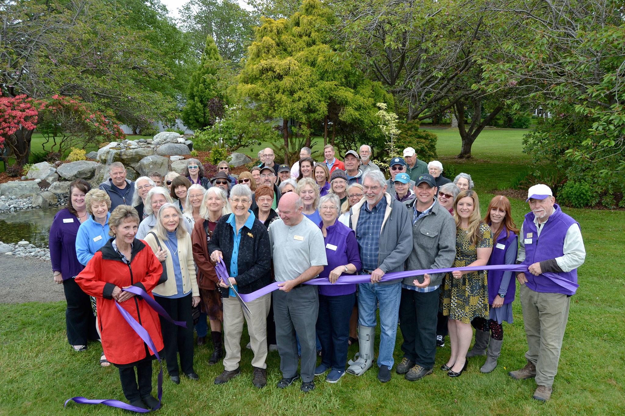 Priscilla Hudson, Sequim Prairie Garden Club member/historian, cuts the ribbon for the refurbished fountain in Pioneer Memorial Park. She’s surrounded by dozens of community members including family members of the Lotzgesell family with Henry Lotzgesell donating a sizable amount in 1965 in honor of his wife Hazel to see the project come to fruition. (Matthew Nash/Olympic Peninsula News Group)