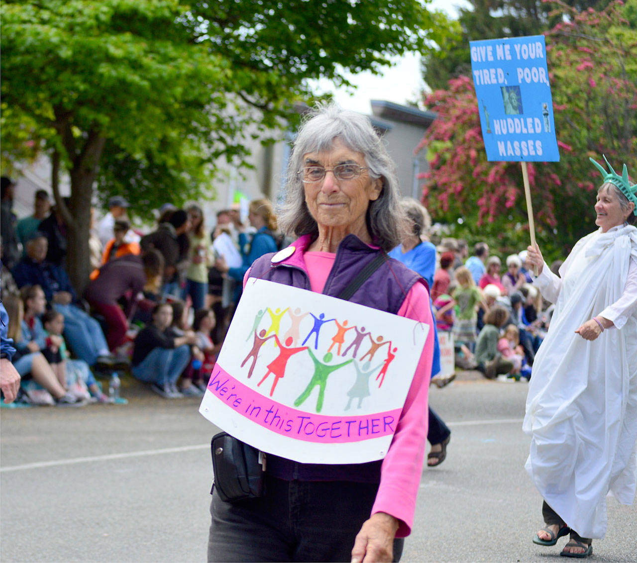 “We’re all in this together,” reads Libby Palmer’s sign, while Katie Franco marches as Lady Liberty in May’s Rhody Grand Parade. The Port Townsend women are members of Jefferson County Immigrants Rights Advocates. (Diane Urbani de la Paz/for Peninsula Daily News)
