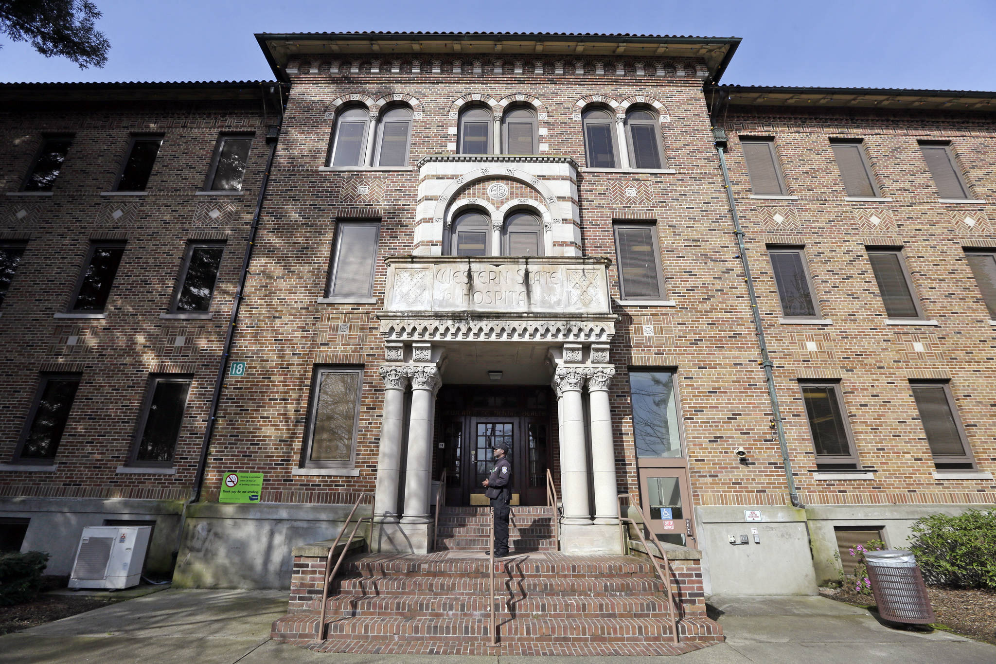 In this file photo taken April 11, 2017, a security officer stands on steps at the entrance to Western State Hospital, in Lakewood, Wash. Hundreds of mentally ill patients at Washington state’s largest psychiatric hospital are forced to live in conditions that do not meet federal health and safety standards, while overworked nurses and psychiatrists say they must navigate a management system that punishes whistleblowers. (AP Photo/Elaine Thompson, File)