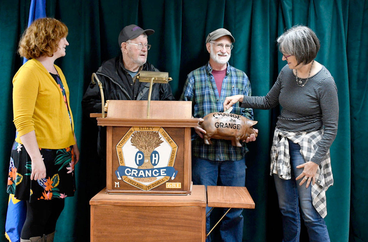 The Chimacum Grange celebrates 100 years of service to the agriculture community with a pancake breakfast Sunday. Feeding the pig bank held by grange Treasurer Al Latham is Katy McCoy, member of the advisory council. Grange events coordinator Tia Taylor, left, and Program Director James Fritz are hoping to raise money to help offset the cost of operating the building, constructed in 1932. (Jeannie McMacken/Peninsula Daily News)