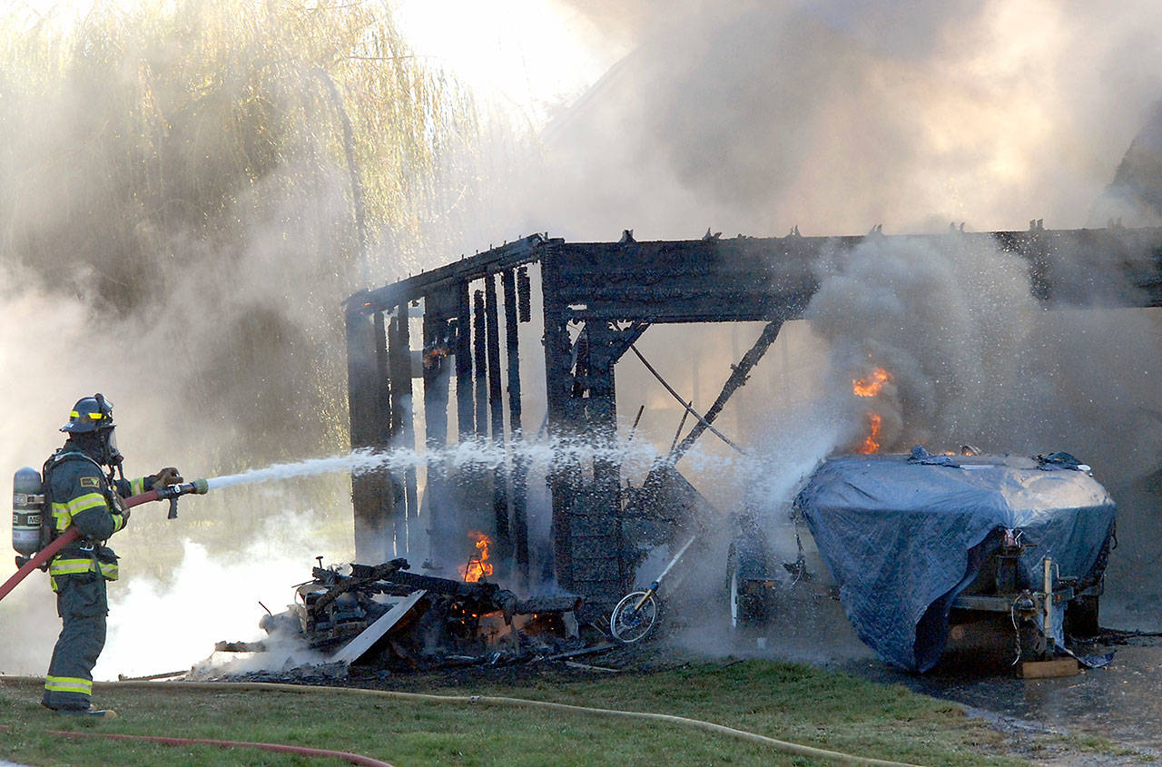 A firefighter from Clallam County Fire District No. 2 sprays water on a fire that destroyed a garage and inflicted heavy damage to a house at 2418 W. Edgewood Drive near the Port Angeles city limits Tuesday. Heat from the blaze also ignited siding of a nearby house at 2414 W. Edgewood Drive, where fire spread into the attic. (Keith Thorpe/Peninsula Daily News)