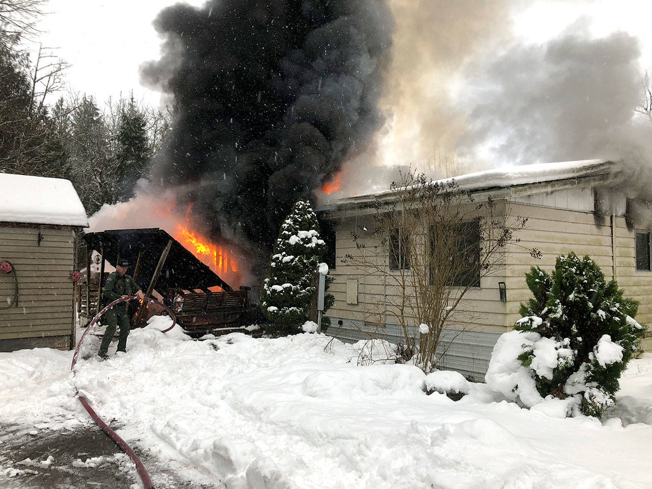 Jefferson County Sheriff’s Deputy Darrin Dotson holds the hose as firefighters respond to a fire in Chimacum on Monday afternoon. (Jefferson County Sheriff’s Office)