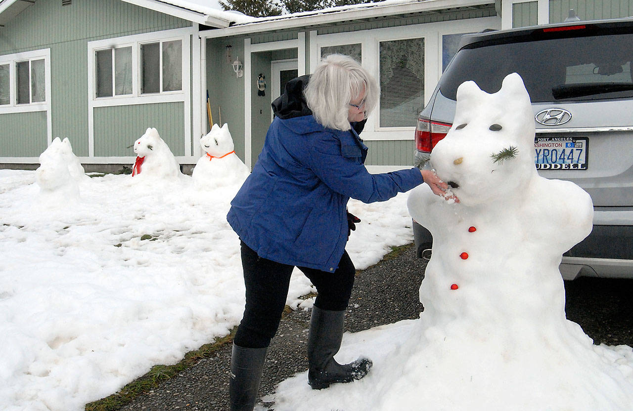 Cindy Sofie adds a handful of snow to touch up one of a series of snow sculptures in front of her home on West 14th Street in Port Angeles on Friday. With temperatures above freezing, she said the frosty creatures were rapidly melting and required maintenance. (Keith Thorpe/Peninsula Daily News)
