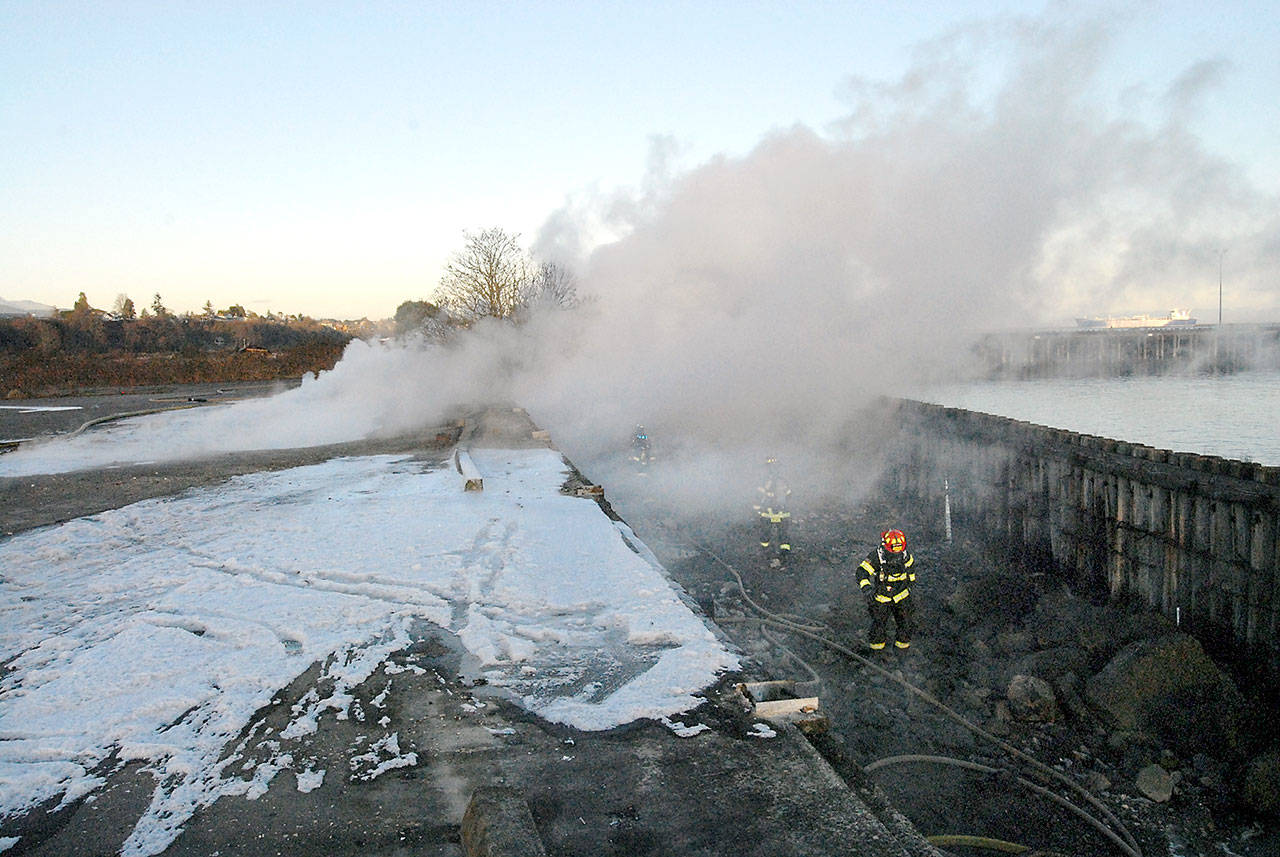 Port Angeles firefighters, with assistance from Clallam County Fire District 2, work at the scene of a fire in pilings Tuesday at the former Rayonier pulp mill site east of downtown Port Angeles. (Keith Thorpe/Peninsula Daily News)