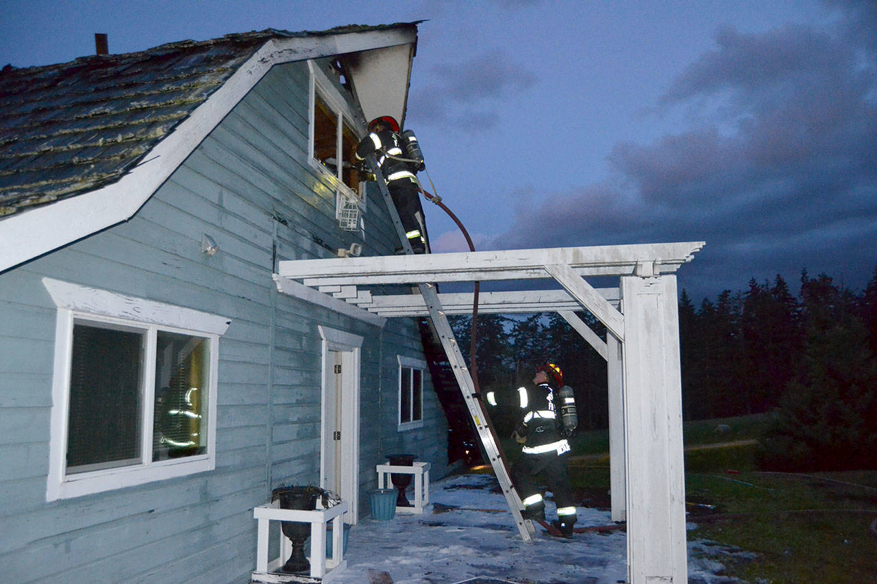 Port Ludlow Fire and Rescue firefighters look for hot spots Friday night in a Gardiner home on the 2000 block of Old Gardiner Road. Fire officials say the cause of the fire remains under investigation. (Matthew Nash/Olympic Peninsula News Group)