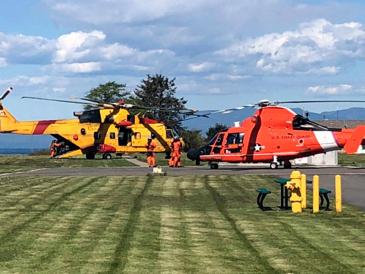 An MH-65 Dolphin helicopter aircrew from U.S. Coast Guard Sector Field Office Port Angeles transfers two patients to a Royal Canadian helicopter aircrew at Neah Bay on Sunday. The Coast Guard aircrew rescued two boaters from a beach near Tsusiat Falls, B.C., after the boaters made a mayday call. (U.S. Coast Guard Sector Field Office Port Angeles)