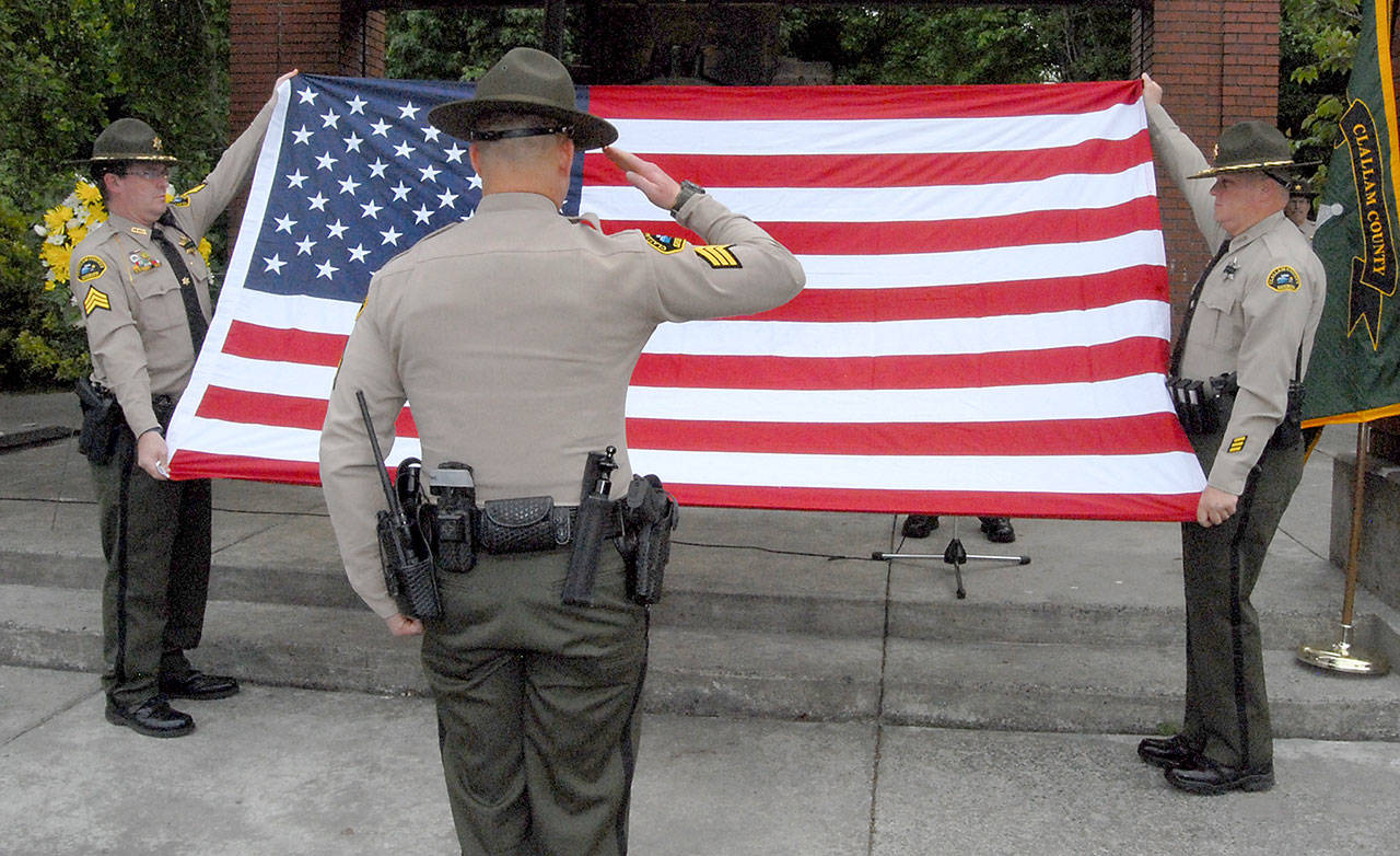 Clallam County Sheriff’s Office Sgt. Brian Knutson, center, salutes a flag held by Sgt. John Keegan, left, and Deputy Don Kitchen during a memorial to fallen law enforcement officers on Friday at Veteran’s Park in Port Angeles. (Keith Thorpe/Peninsula Daily News)