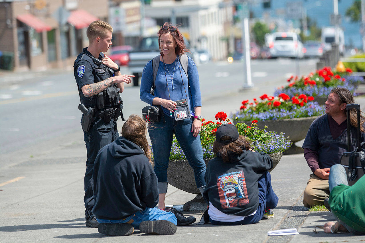 Port Angeles Police Department Officer Jackson VanDusen and Community Change Agent Amy Miller, of the REdisCOVERY program, talk with people at Veterans Memorial Park. (Jesse Major/Peninsula Daily News)