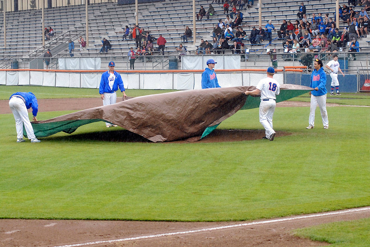 Lefties players spread a tarp over the pitcher’s mound as heavy rain pours down on Port Angeles Civic Field on Wednesday evening. The rainstorm drenched the stadium, and coaches and game officials declared the field unplayable, forcing cancellation of the Lefties game against the Corvallis Knights in the top of the second inning with no score. Keith Thorpe/Peninsula Daily News