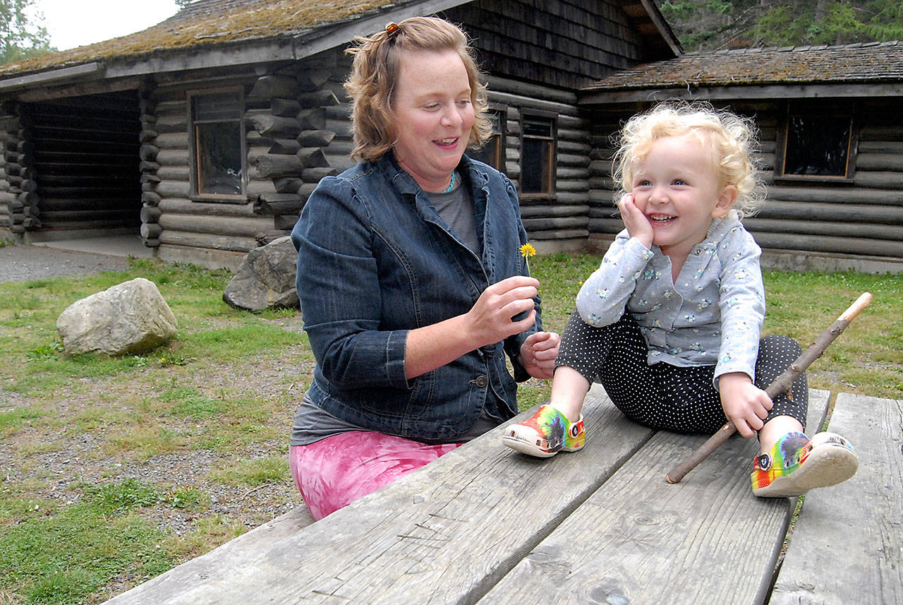 Anya Samawicz of Port Angeles plays with a dandelion with her daughter, Sunny Eckenberg, 2 1/2, outside the former Loomis Tavern building at Lincoln Park, the site where she plans to start an outdoor preschool for pre-kindergarten children. (Keith Thorpe/Peninsula Daily News)