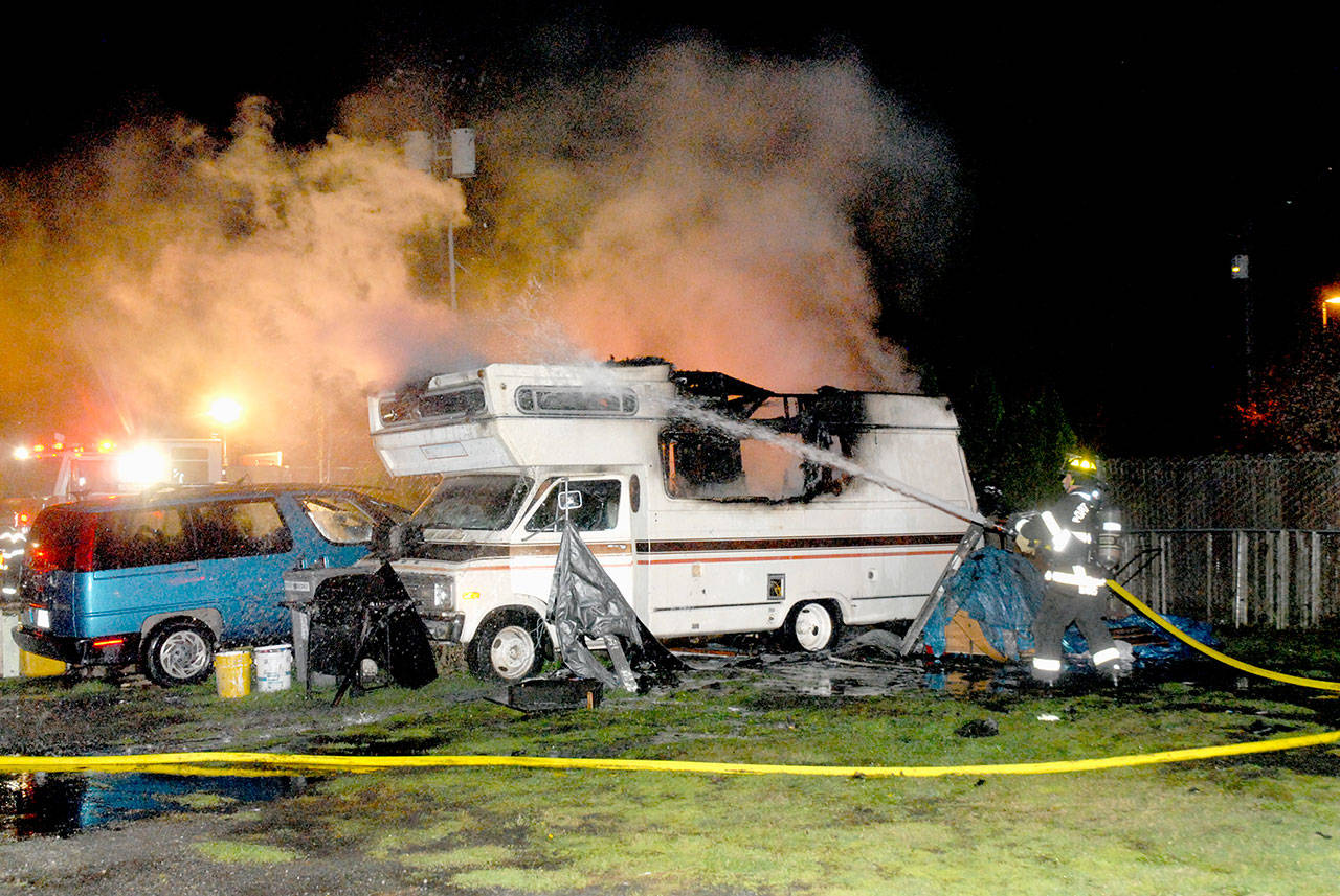 A Port Angeles firefighter douses hot spots on a recreational vehicle that caught fire near the alley East Front Street. (Keith Thorpe/Peninsula Daily News)