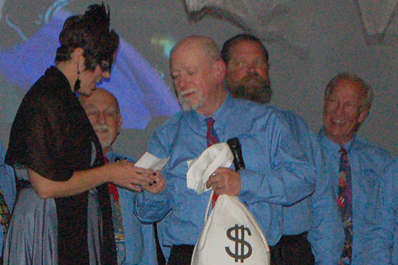 The Olympic Peninsula Men’s Choir presents Clallam Mosaic with a $500 donation before starting its performance at the Mosaic Masquerade fundraiser. (Conor Dowley/Olympic Peninsula News Group)