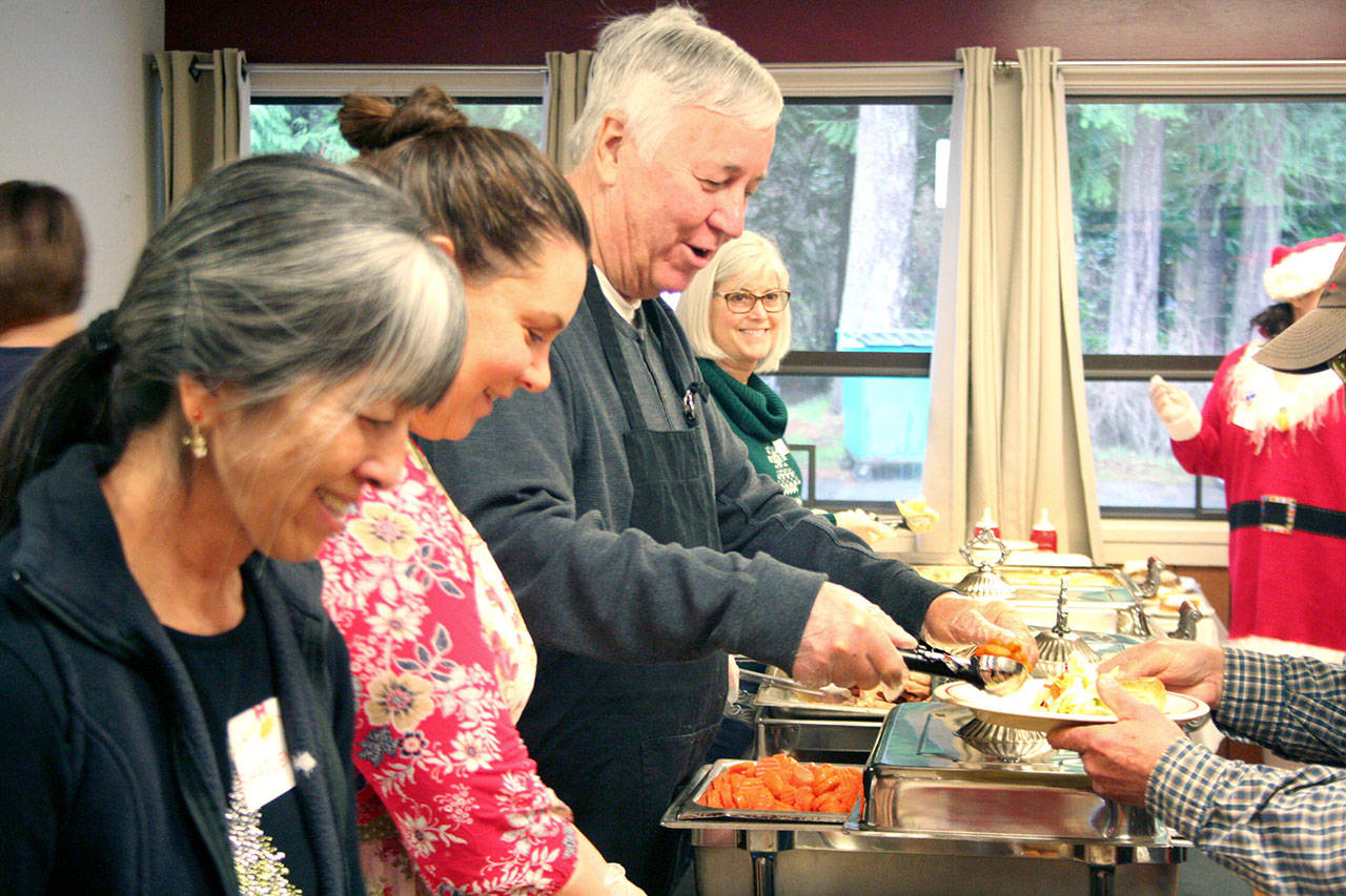John Carter, center, serves carrots on Christmas Day during the Tri-Area Community Meals dinner on Wednesday. He went to purchase a case of whipped cream earlier in the day at Safeway, and a man he didn’t know behind him in line picked up the $60 tab. (Brian McLean/Peninsula Daily News)