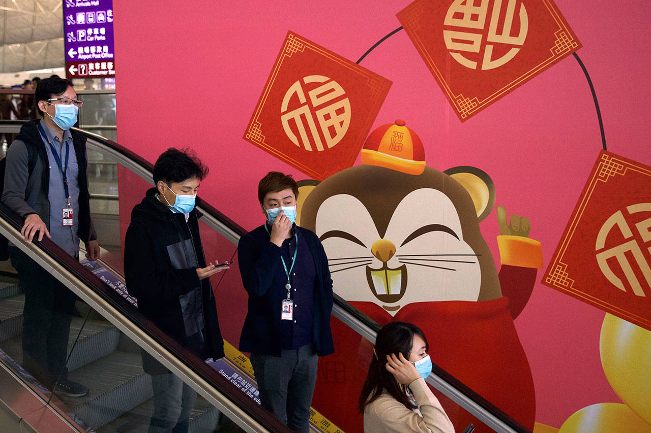 People wear face masks as they ride an escalator at the Hong Kong International Airport in Hong Kong, Tuesday, Jan. 21, 2020. Face masks sold out and temperature checks at airports and train stations became the new norm as China strove Tuesday to control the outbreak of a new coronavirus that has reached four other countries and territories and threatens to spread further during the Lunar New Year travel rush. (Ng Han Guan/Associated Press)