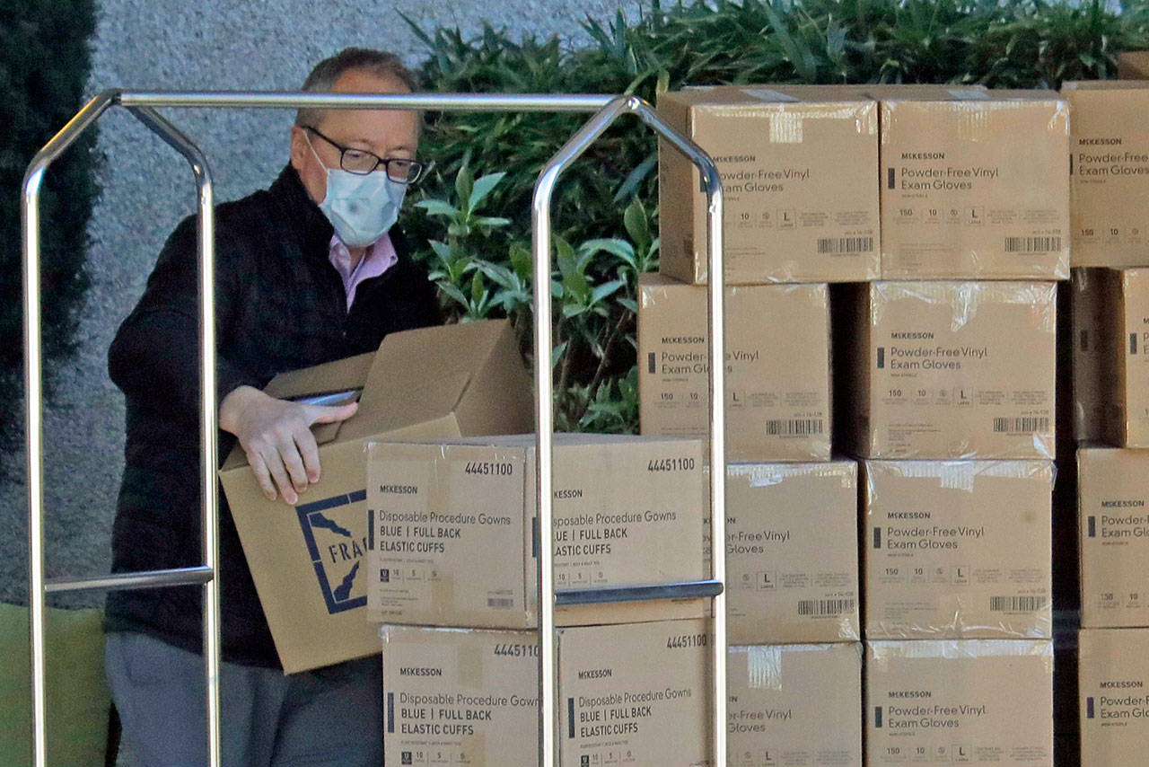 A worker wears a mask as he loads new supplies of gloves, gowns and other protective gear onto a cart at the Life Care Center in Kirkland on Monday, March 9, 2020, near Seattle. The nursing home is at the center of the outbreak of the COVID-19 coronavirus in Washington state. (Ted S. Warren/The Associated Press)