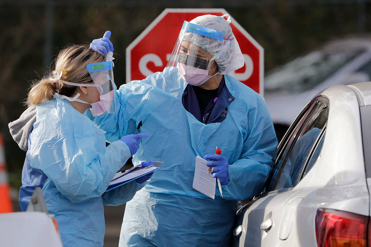 Theresa Malijan, a registered nurse, right, talks with medical assistant Miriam Fuentes as Malijan prepares to take a nasopharyngeal swab from a patient at a drive-through COVID-19 testing station for University of Washington Medicine patients Tuesday, March 17, 2020, in Seattle. The appointment-only drive-through clinic began a day earlier. Washington leads the country in the number of deaths, with most being associated with a nursing home in Kirkland. By Monday, the number of positive cases topped 900. (Elaine Thompson/The Associated Press)