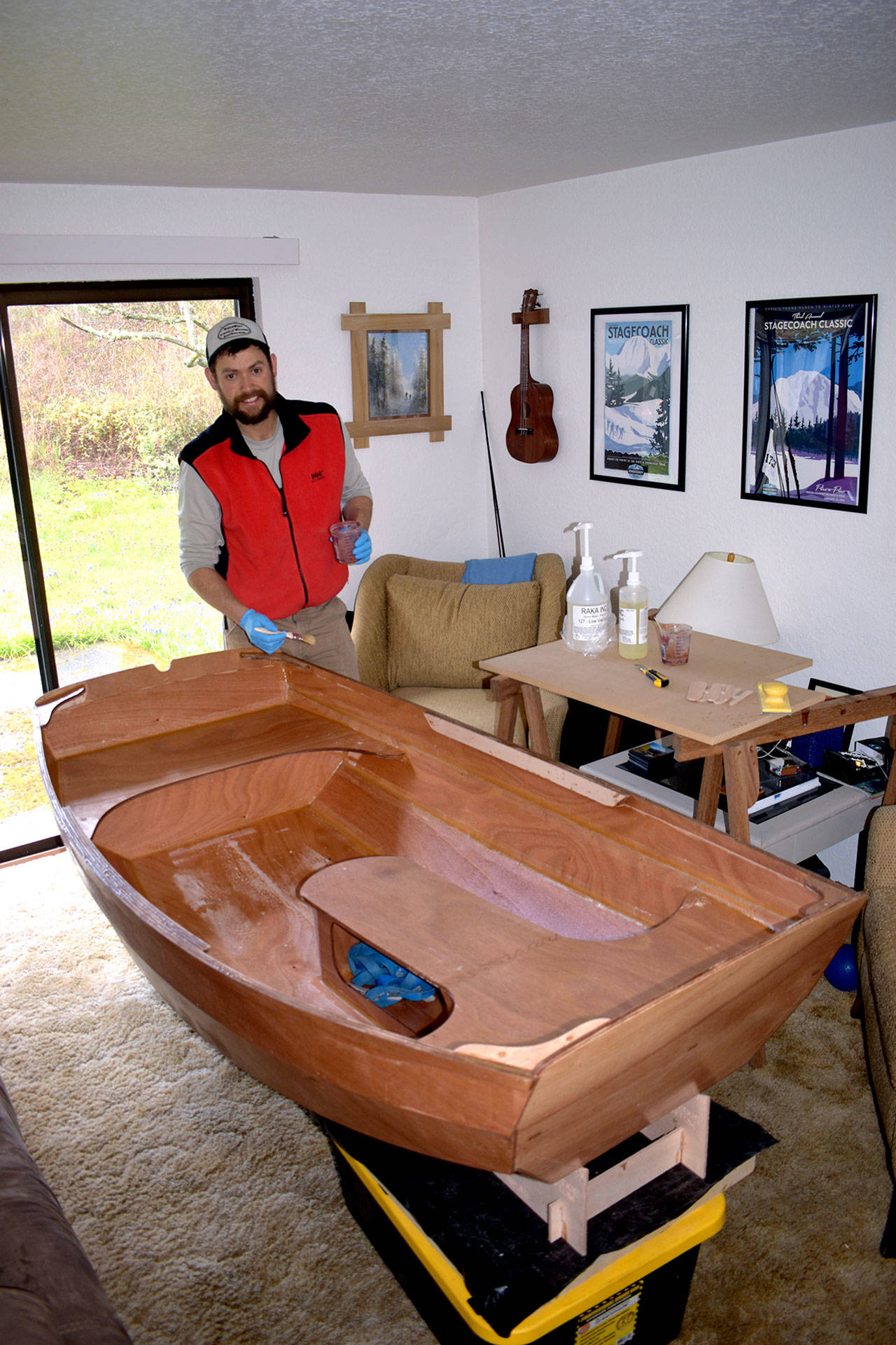 Northwest Maritime Center instructor Joel Arrington stands in his living room with a completed test build of the Portage Pram boat kit that his students will be constructing in the online course starting on April 20. (Kate Philbrick)