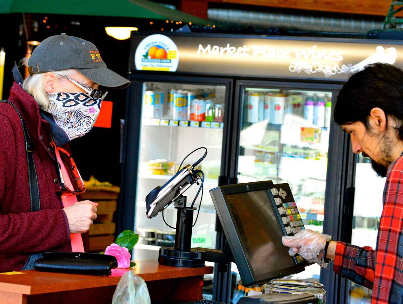 Aldrich’s Market cashier Tim Mata, right, rings up a lunchtime shopper Thursday, April 9, 2020. (Diane Urbani de la Paz/for Peninsula Daily News)