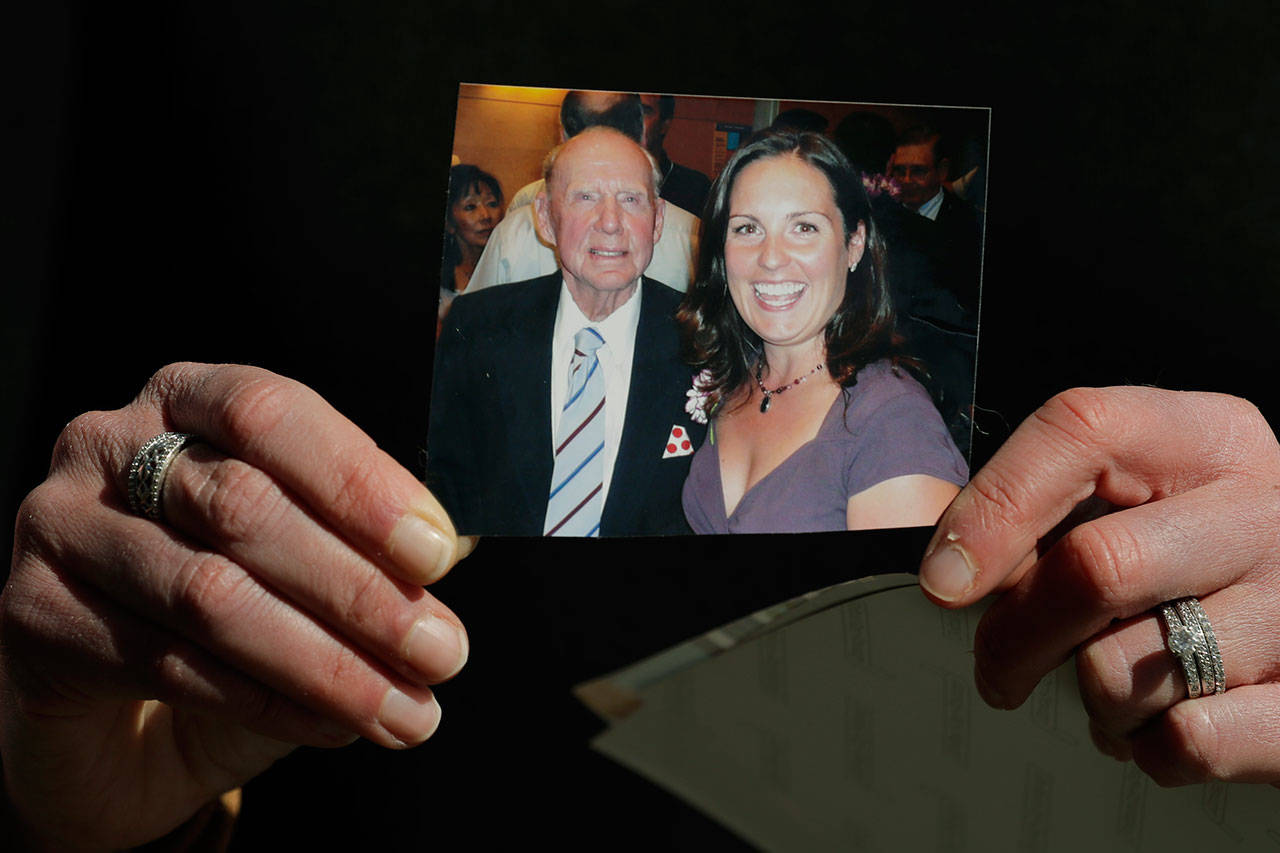 In this Wednesday, April 8, 2020, photo, Kelly Adsero holds a family photo of her grandfather Bill Chambers with her on the day she graduated as a physician’s assistant in 2007. Chambers, 97, died March 14, 2020, at an adult family home where he lived with four other World War II veterans. He wasn’t obviously ill, but tested positive for the new coronavirus after he died. (AP Photo/Ted S. Warren)