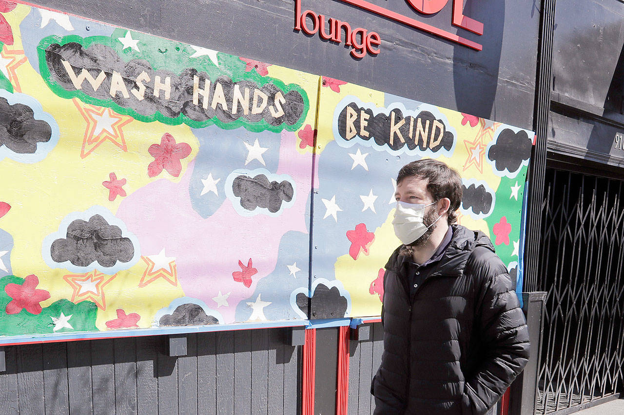 A pedestrian walks past artwork painted on plywood covering a business closed during the coronavirus outbreak Thursday, April 16, 2020, in Seattle. (Elaine Thompson/The Associated Press)