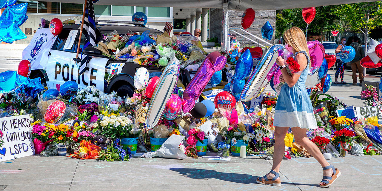 A memorial for Bothell Police Officer Jonathan Shoop, killed in the line of duty on Monday evening, grows on top of and around a Bothell Police Car parked at Bothell City Hall on Wednesday in Bothell. (Mike Siegel/The Seattle Times via The Associated Press)