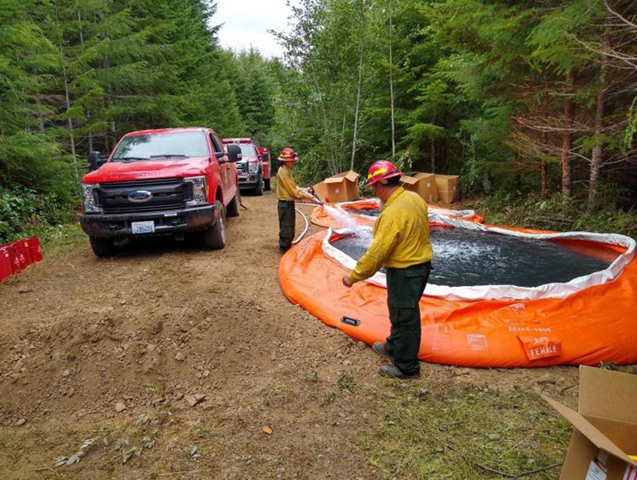 Firefighters fill portable water tanks on top of the ridge above the East Beach Road Fire. These tanks allow firefighters to have a cache of water to draw from to help cool down and put out hot spots around the edges of the fire above Lake Crescent. (Photo courtesy of Olympic National Park)