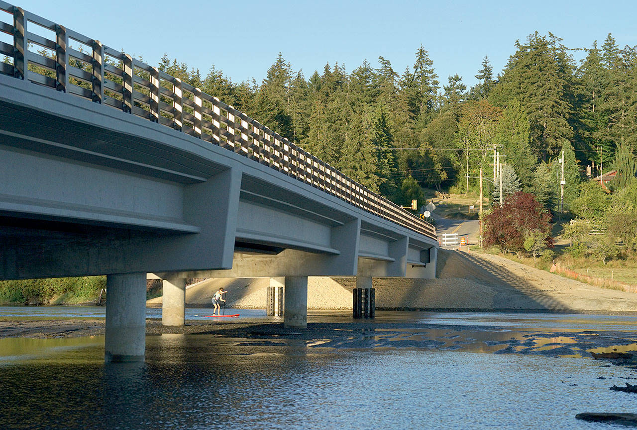 River Kisler, 17, of Chimacum rides his paddleboard underneath the newly constructed Kilisut Harbor Bridge on Monday evening, mere days after water began flowing for the first time through a newly dredged channel between Oak Bay and Kilisut Harbor’s Scow Bay. “It’s so cool to see this finally come to fruition,” Kisler said. (Nicholas Johnson/Peninsula Daily News)