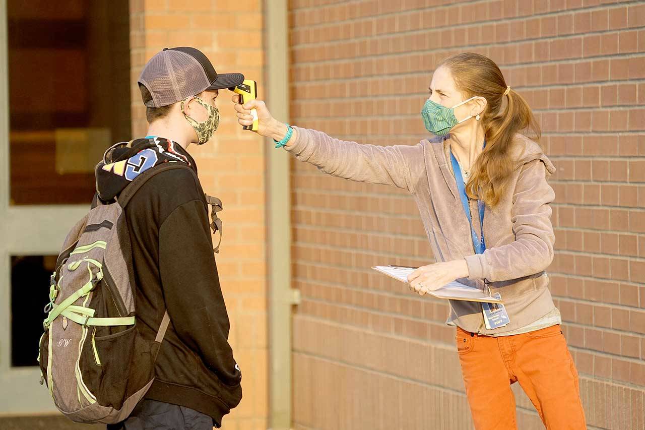 Paraeducator Alice Fraser, right, checks seventh-grader Garret Warren’s temperature Tuesday morning outside Blue Heron Middle School in Port Townsend. (Nicholas Johnson/Peninsula Daily News)