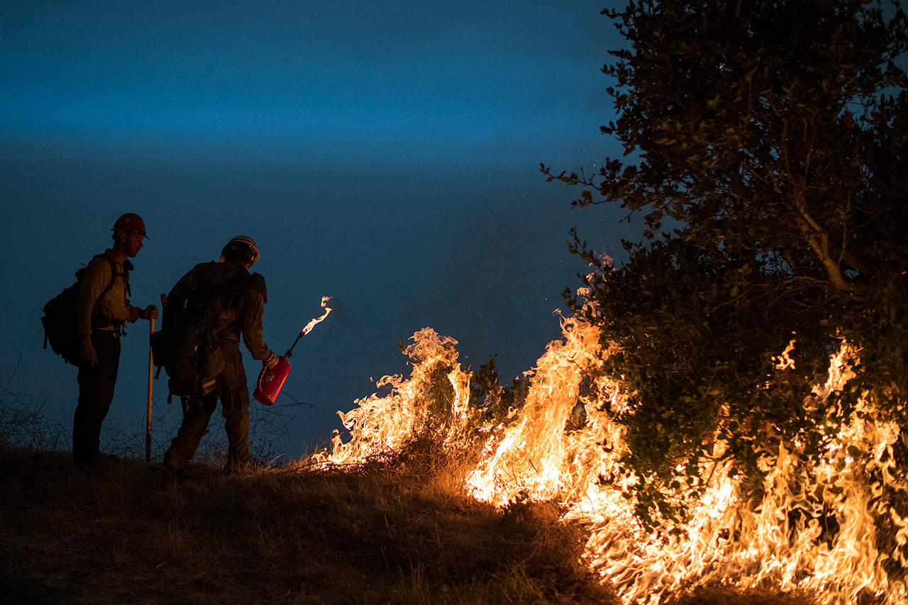 In this Sept. 11, 2020, file photo, firefighters light a controlled burn along Nacimiento-Fergusson Road to help contain the Dolan Fire near Big Sur, Calif. Rain showers fell Thursday, Sept. 24, 2020, on the northwestern edges of fire-ravaged California but forecasters warned residents to not be fooled: a new round of hot, dry and windy weather is expected by the weekend. (Nic Coury/Associated Press file)