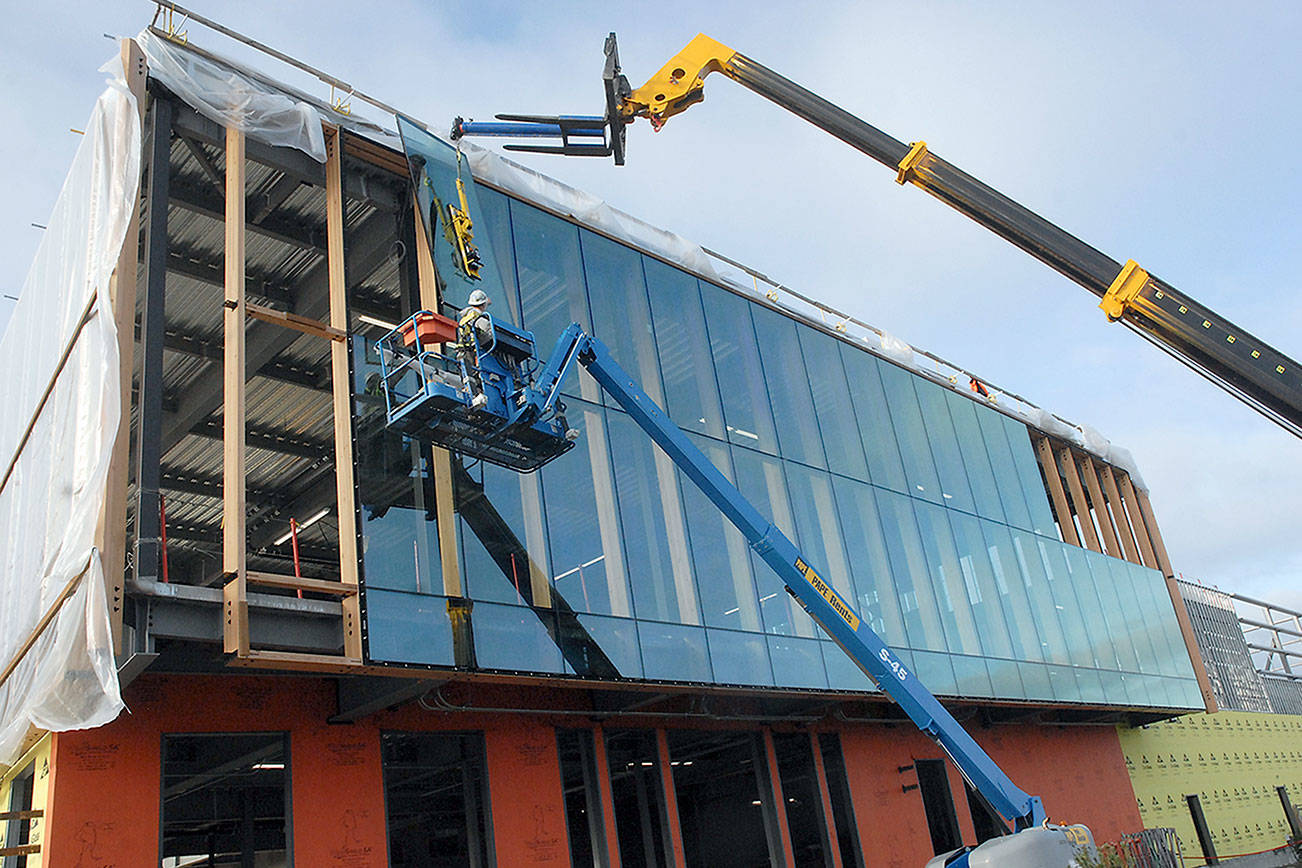 Keith Thorpe/Peninsula Daily News
Crews install plate glass windows on the northeast face of the new Field Arts & Events Hall at the Port Angeles Waerfront Center on Tuesday. The 41,000-square-foot structure which will include an art gallery, performance hall, conference center and coffee shop, was scheduled to be completed by summer 2021, will be put on a construction hold in January as organizers attempt to secure more funding to complete the project after previous fundraising projections fell short due to the COVID-19 pandemic.