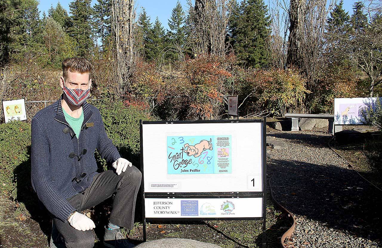 Scott Bahlmann, youth and teen services librarian at the Jefferson County Library, kneels next to the start of the storywalk outside the library. Bahlmann, along with public services manager Chris HoffmanHill, curated the three storywalks that are now located throughout Jefferson County. (Zach Jablonski/Peninsula Daily News)