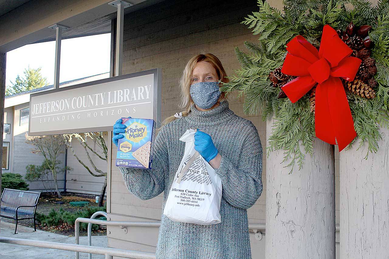 Quintana Kelley, library assistant at the Jefferson County Library, holds the gingerbread house-making kit that the library is passing out for its annual edible house-building competition. Registration to pick up the free kits closes Saturday, and photos of the finished houses are due by Dec. 13. (Zach Jablonski/Peninsula Daily News)