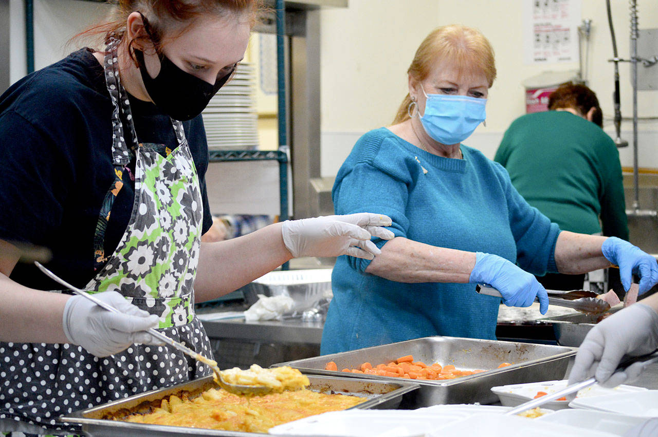 Volunteers Mya Lindstrom, left, and Judy Robinett direct the carrots and scalloped potatoes through the assembly line during the Tri-Area Community Center’s Christmas dinner on Friday. (Diane Urbani de la Paz/Peninsula Daily News)