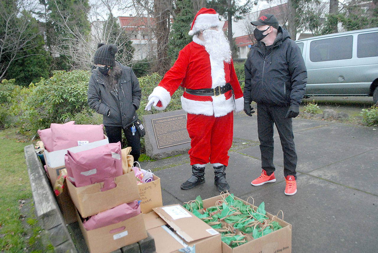 Santa portrayed by shelter coordinator Casey Sawyer for Serenity House of Clallam County, gives gift-giving directions to Serenity House client Roger Smith, right, as Viola Ware of the Rediscovery Program looks on during meal and gift distribution at Veterans Park on Christmas Day in Port Angeles. (Keith Thorpe /Peninsula Daily News)