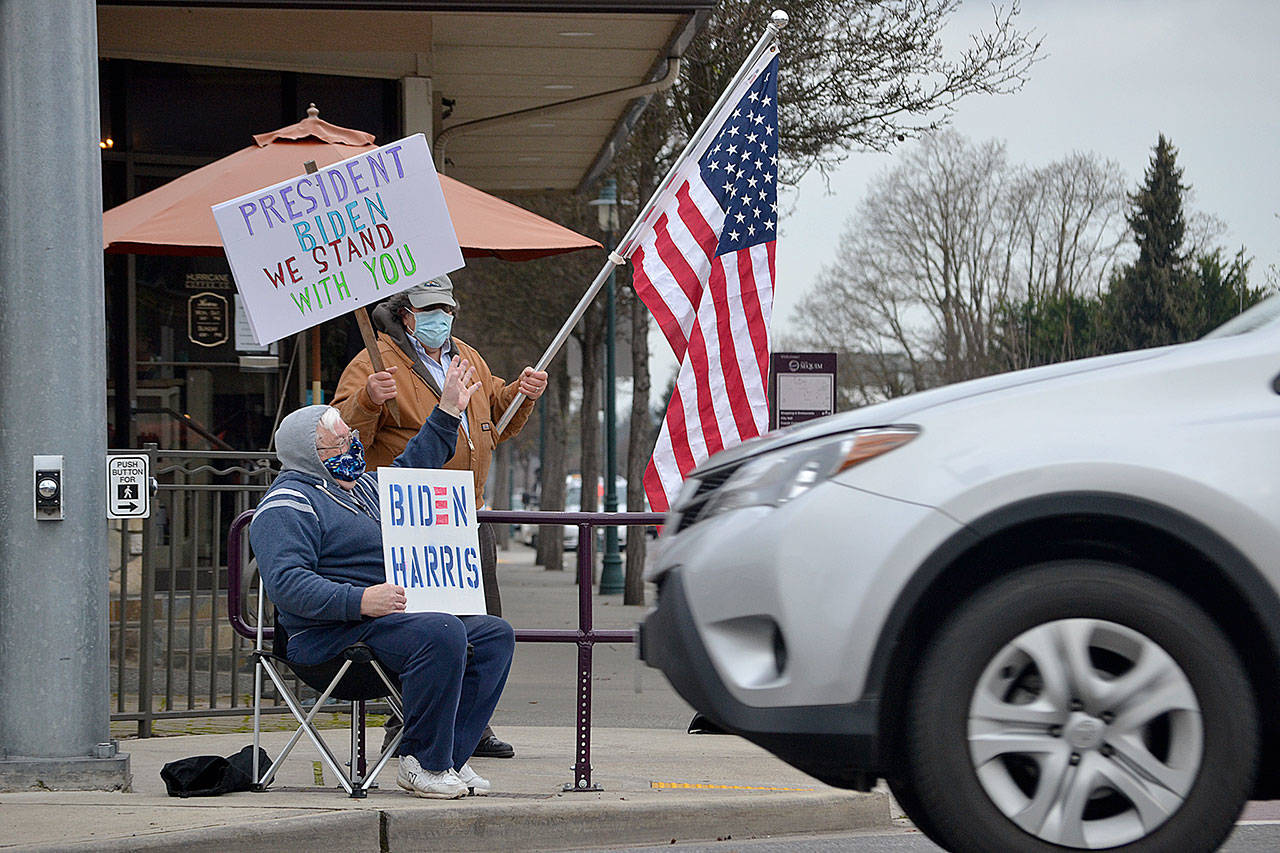 Steve Downer and Brian Grad, both of Sequim, wave to drivers on Wednesday as they celebrate the inauguration of President Joe Biden and Vice President Kamala Harris. “I’m relieved,” Downer said of the inauguration. He hopes their first steps will be to address COVID-19, the economy and environment. (Matthew Nash/ Olympic Peninsula News Group)