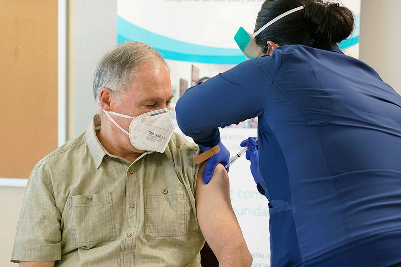 Washington Gov. Jay Inslee, left, gets the first shot of the Moderna COVID-19 vaccine, Friday, Jan. 22, 2021, from Elizabeth Smalley, right, a medical assistant at a Sea Mar Community Health Center in Olympia, Wash. Inslee's wife Trudi also received the first dose of the vaccine. (AP Photo/Ted S. Warren)