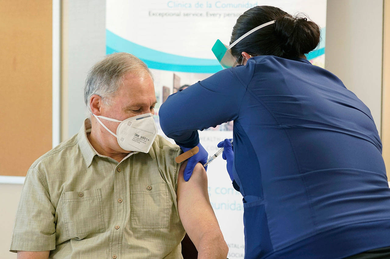 Gov. Jay Inslee, left, gets the first shot of the Moderna COVID-19 vaccine Friday from Elizabeth Smalley, right, a medical assistant at a Sea Mar Community Health Center in Olympia. Inslee’s wife Trudi also received the first dose of the vaccine. (AP Photo/Ted S. Warren)