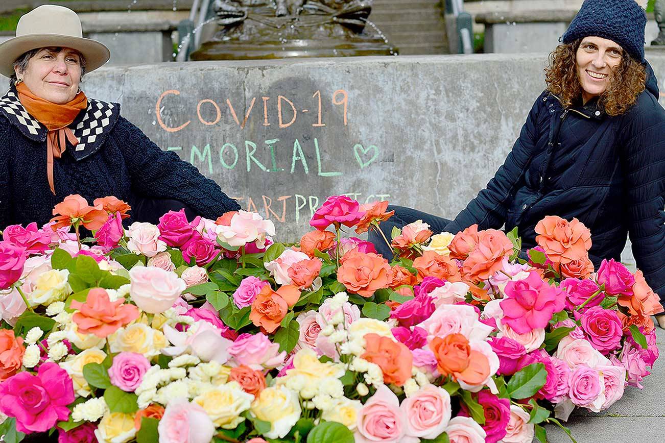 Lisa Leporati, left, and Lexi Koch built a garland of roses beneath the Haller Fountain in downtown Port Townsend on Monday. The flowers were placed in honor of the people lost to COVID-19 during the past year. (Diane Urbani de la Paz/Peninsula Daily News)