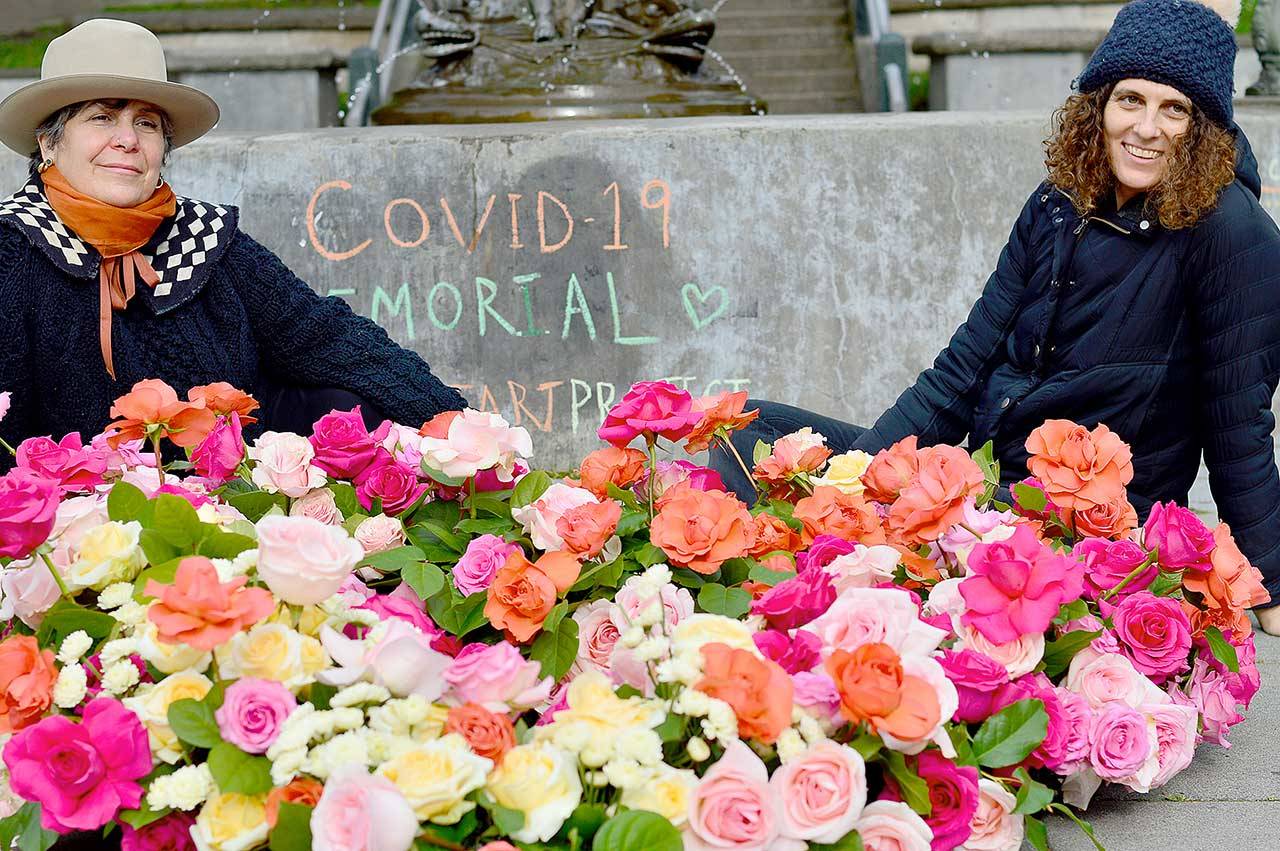 Lisa Leporati, left, and Lexi Koch built a garland of roses beneath the Haller Fountain in downtown Port Townsend on Monday. The flowers were placed in honor of the people lost to COVID-19 during the past year. (Diane Urbani de la Paz/Peninsula Daily News)