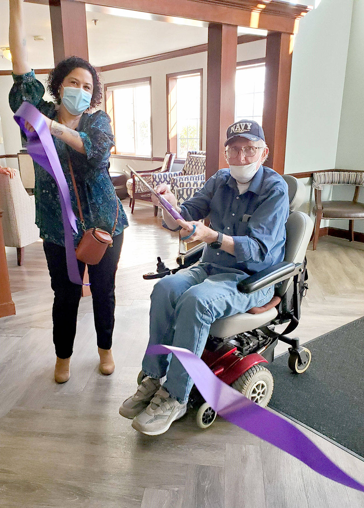 Sinclair Place resident Martin Arnold cuts the ribbon to mark the start of the the senior living facility’s Freedom Ceremony. The ceremony marks the fact that 100 percent of the residents have been vaccinated which allows the facility to ease rules regarding movement out into the community. Pictured on the left is Victorya Rivera, community relations manager at Sinclair Place.