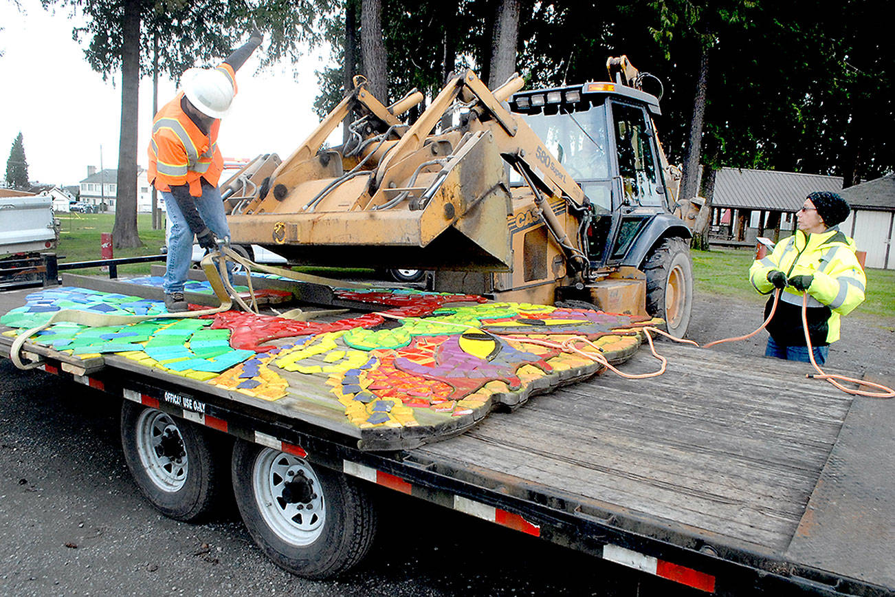 Port Angeles Parks and Recreation worker Darryl Anderson, left, signals to bulldozer operator Leon Leonard as fellow employee Brooke Keohokalole curls up a guide rope after the dragon mosaic from the Dream Playground at Erickson Playfield is lowered onto a trailer earlier this week in Port Angeles. Demolition has begun on the mostly wooden playground, originally built by volunteer labor in September 2002, to make way for modernized playground equipment later this year. The dragon, which once had a playground slide coming from its nose, will be put into storage and later incorporated into the new playground. (Keith Thorpe /Peninsula Daily News)