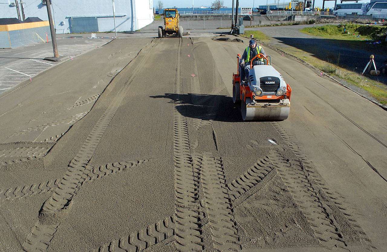 Richard Brandt of Lakeside Industries uses a steam roller on a layer of sand Thursday to create a level surface that will become the base for a temporary ice skating rink in a city parking lot along Front Street in downtown Port Angeles. The rink will be the centerpiece for the annual Port Angeles Ice Village, which would normally be held in the winter months, but was moved to spring because of restrictions imposed by COVID-19. Skating is scheduled to begin on March 19 and run through April 18. (Keith Thorpe/Peninsula Daily News)