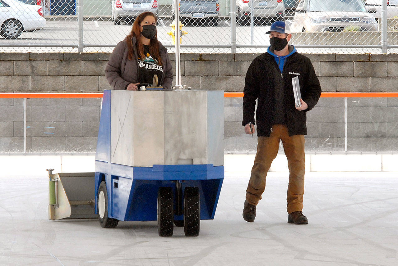Leslie Robertson, events manager for the Port Angeles Regional Chamber of Commerce, gets a refresher course in operating an ice surfacing machine led by J.D. Uhls of Ice-America on Thursday in preparation for today’s opening of the Port Angeles Winter Ice Village. (Keith Thorpe/Peninsula Daily News)