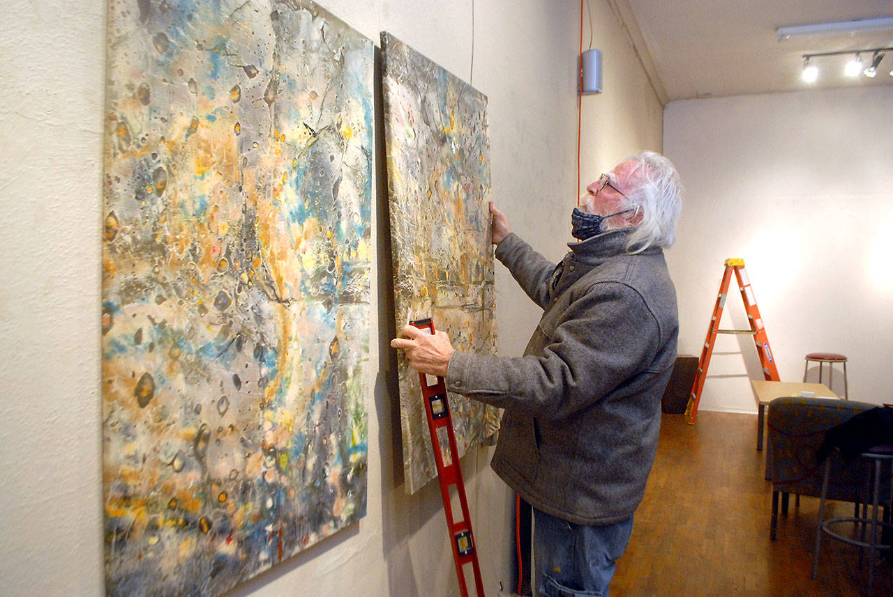 Bob Stokes, owner of Studio Bob in Port Angeles, hangs artworks on the wall of his art and music venue on Wednesday in preparation for Friday’s “Save the Bob” live-streaming music fundraiser. (Keith Thorpe/Peninsula Daily News)