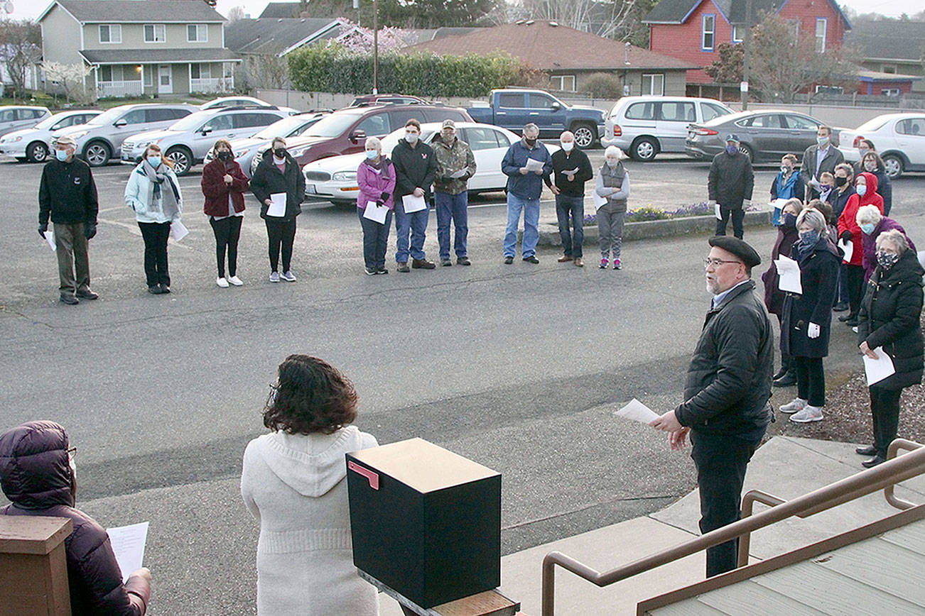 The First Presbyterian Church of Port Angeles held an Easter Sunrise Service modified to meet COVID-19 protocols. Almost 50 worshippers gathered in a circle near the back entrance of the church at 7 a.m. in 40-degree but sunny weather. The group sang songs and heard the story of Jesus' resurrection. The Rev. Matt Paul, in beret, lead the service while Bruce Emery led the music. (Dave Logan/for Peninsula Daily News)